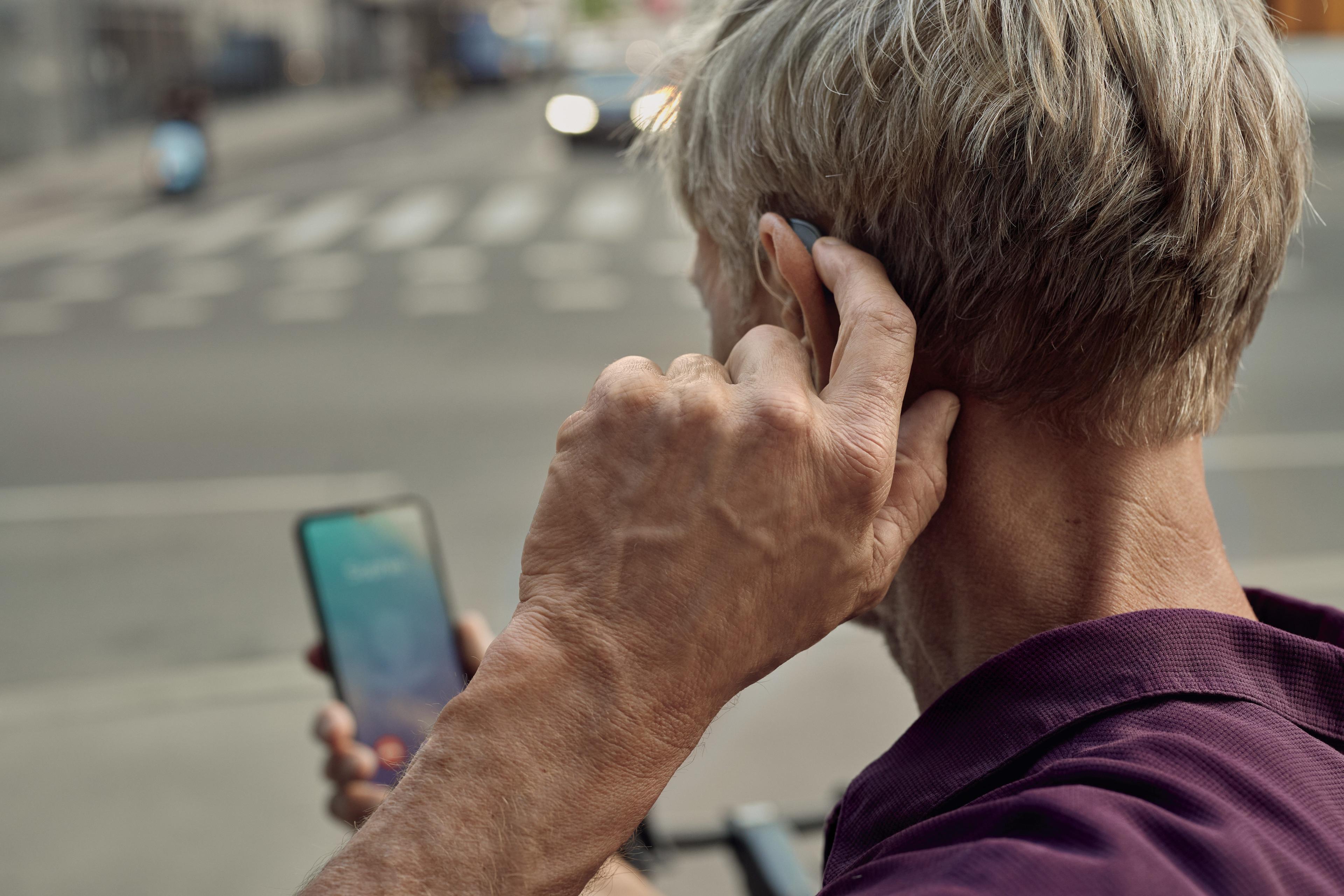 Mann greift sich hinters Ohr und verbindet sein Hörgerät mit seinem Smartphone
