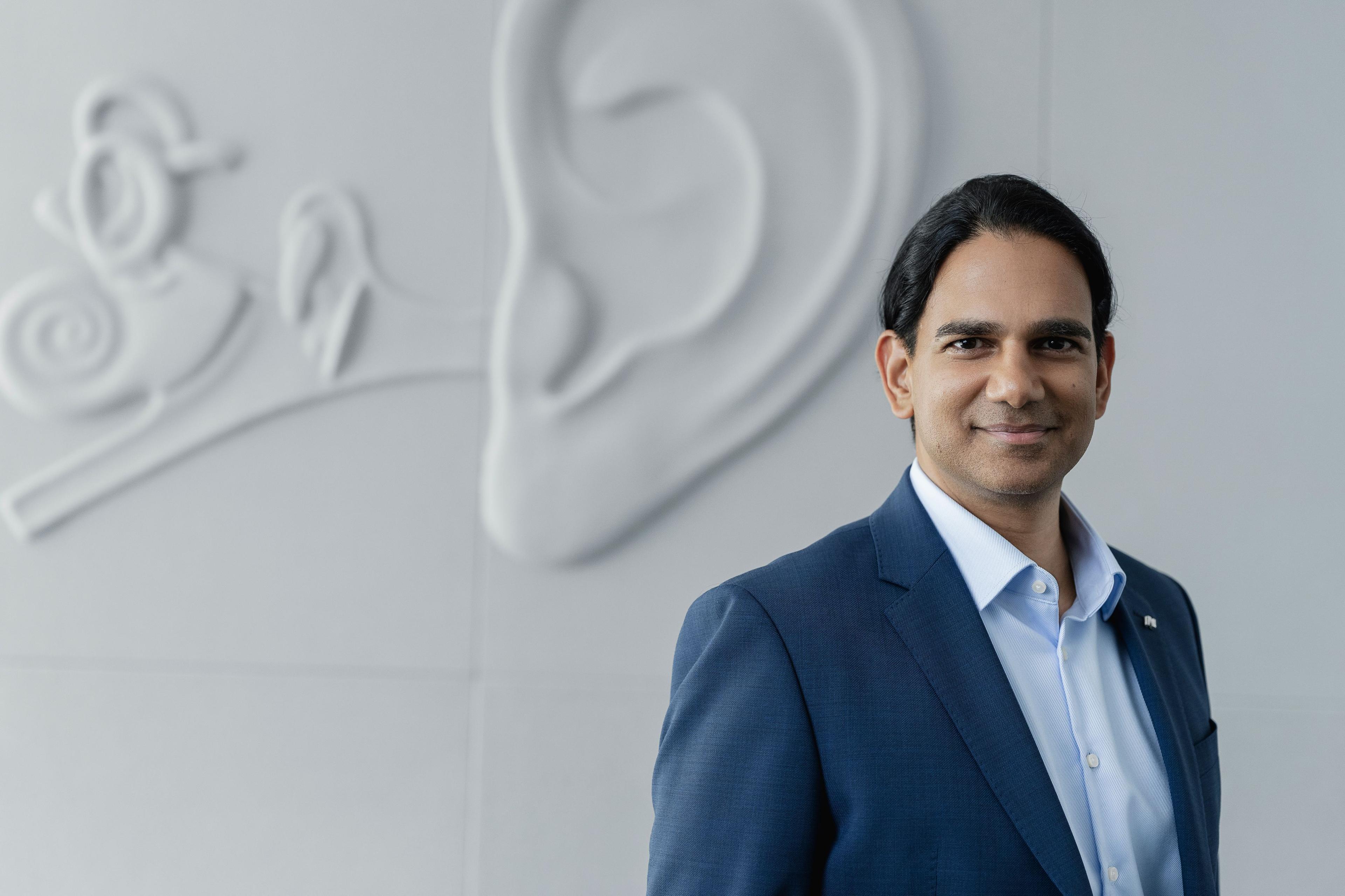 CMO der Neuroth-Gruppe Rabindra Rao steht vor grauer Ohrenwand