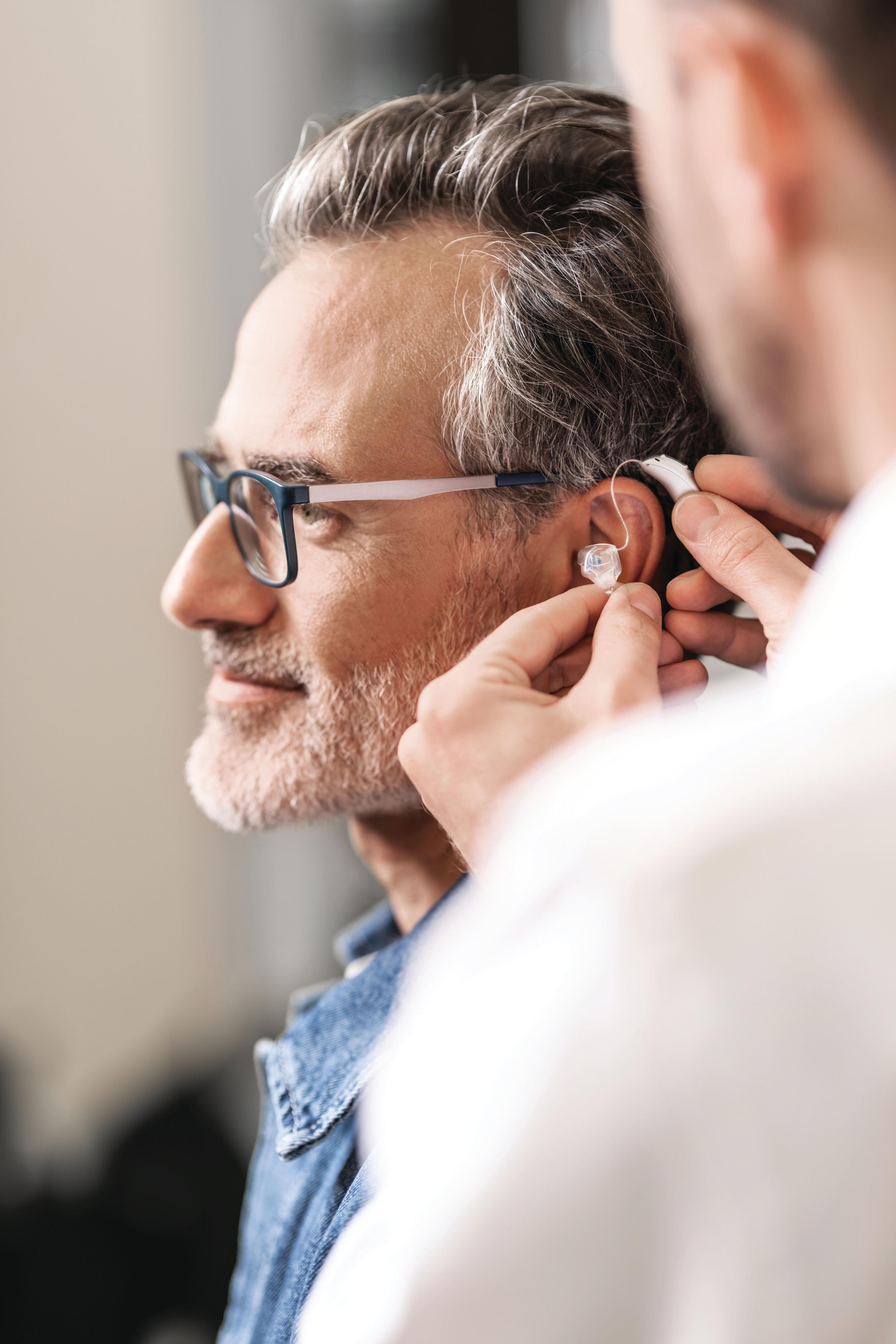 Mann mit Brille bekommt Hörgerät hinters Ohr