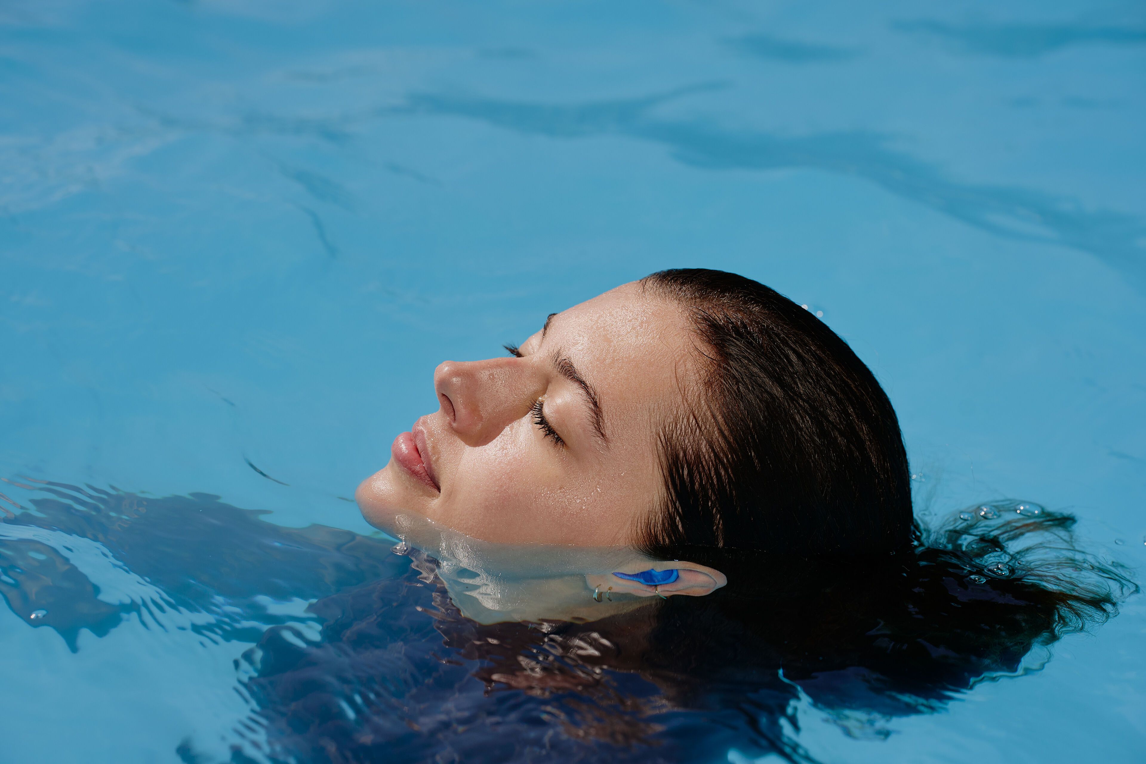 Junge Frau mit Gehörschutz taucht aus dem Wasser auf